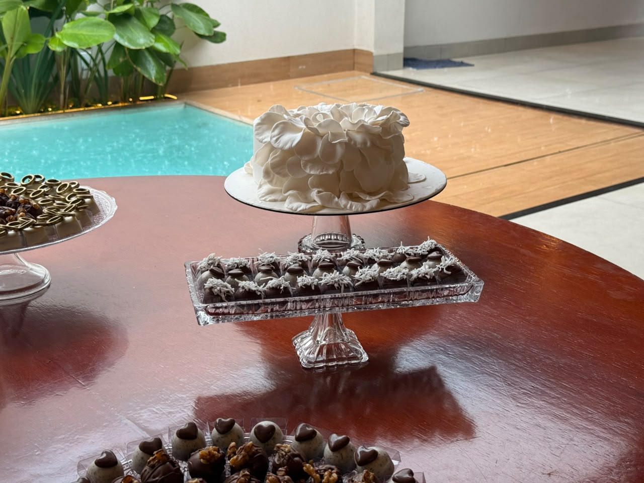 Mesa de bolo e doces montada ao lado da piscina em um evento